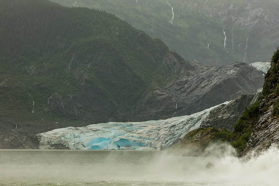 The blue-white face of Mendenhall Glacier meeting the lake below forested mountains