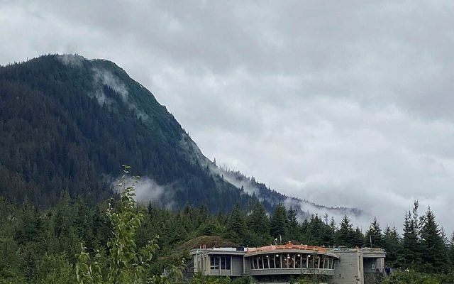 The Mendenhall Glacier Visitor Center on a forested ridge below misty mountains