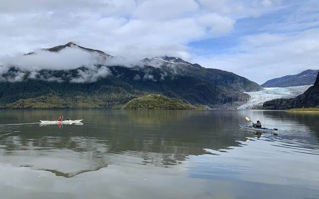Two kayakers paddling on calm Mendenhall Lake with the glacier in the distance