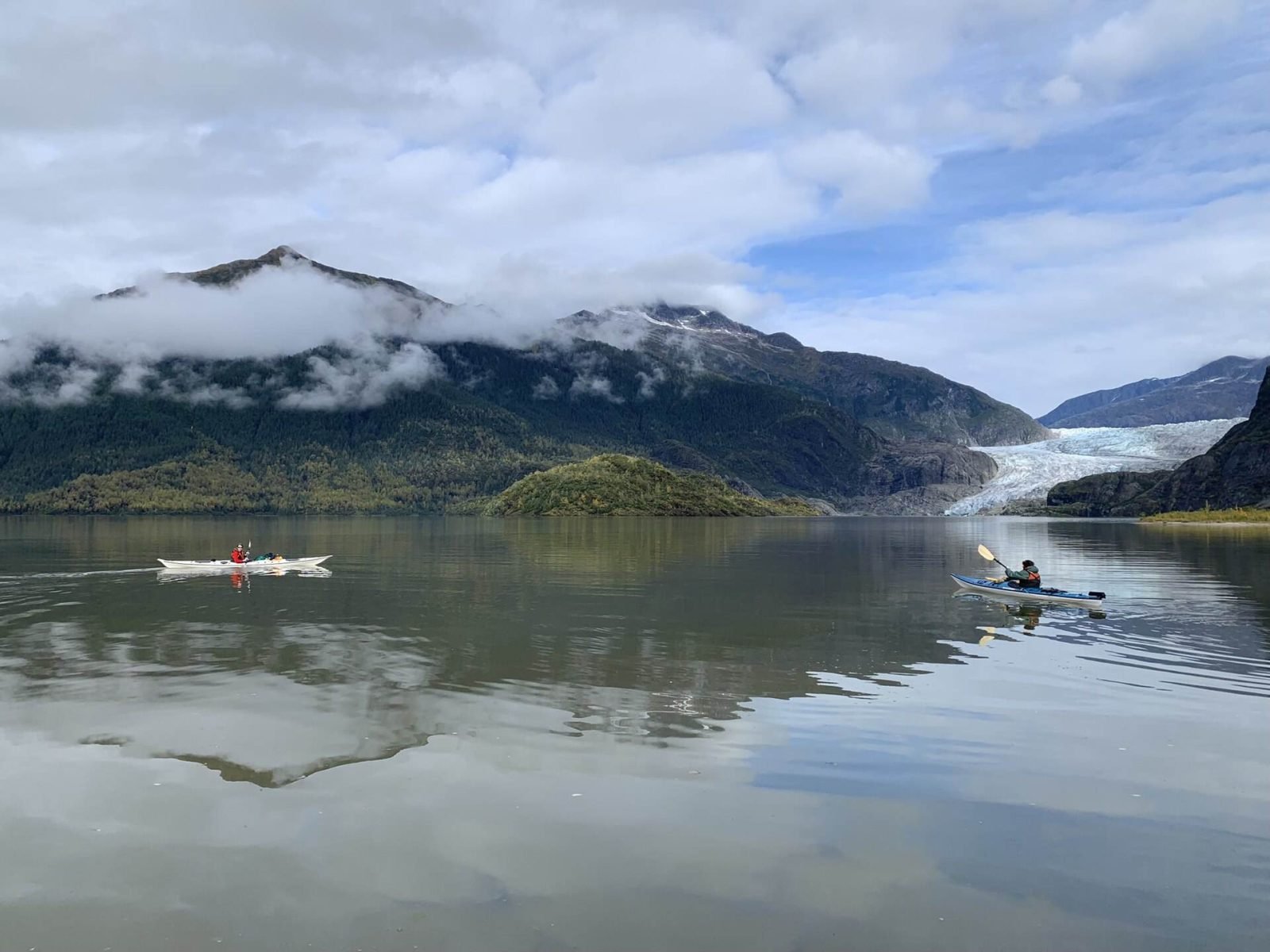 Two kayakers paddling on calm Mendenhall Lake with the glacier in the distance