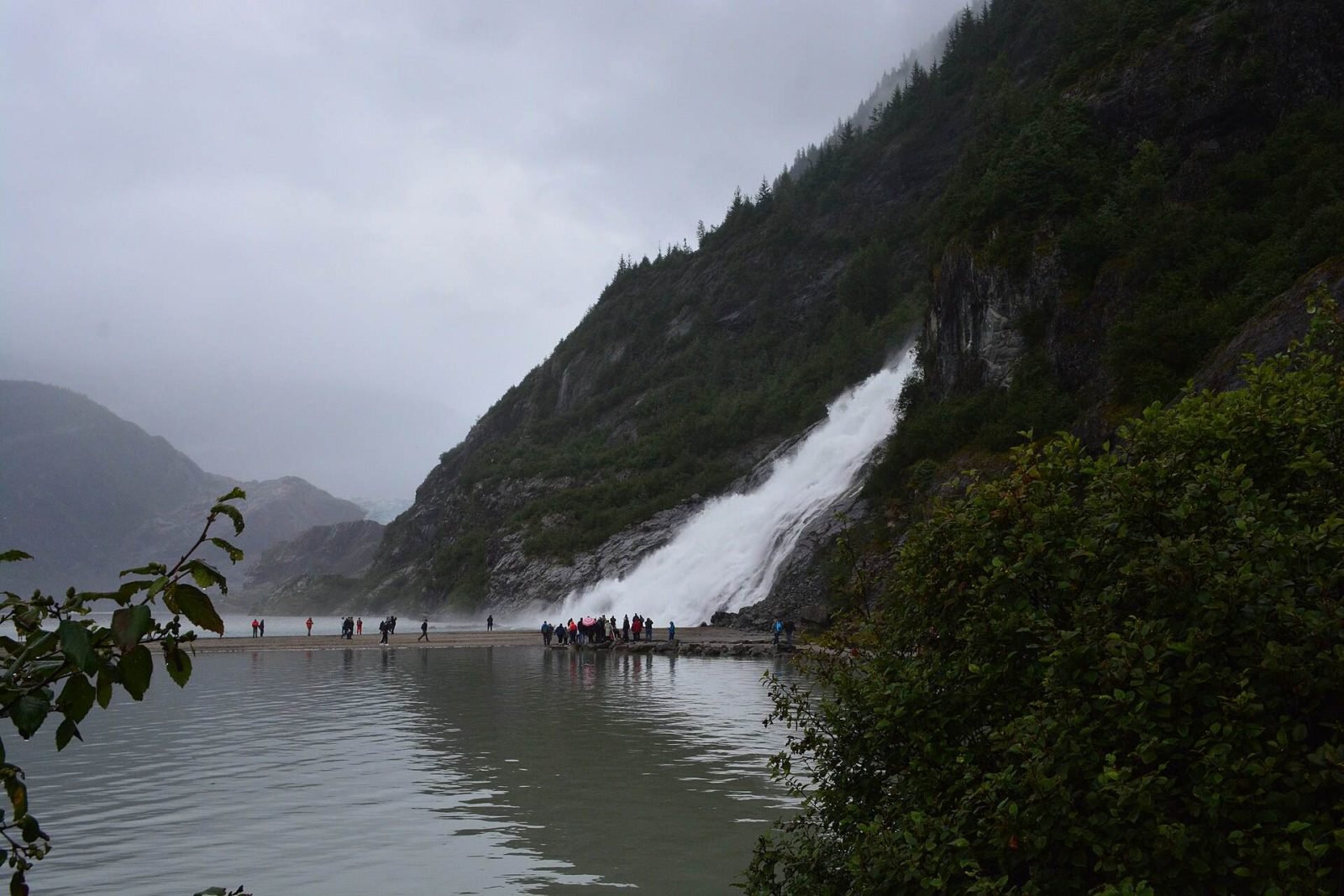 Nugget Falls pouring into Mendenhall Lake below a steep forested mountainside