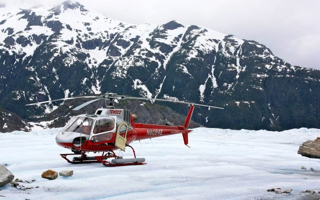 A red helicopter parked on the snow of Mendenhall Glacier below jagged peaks
