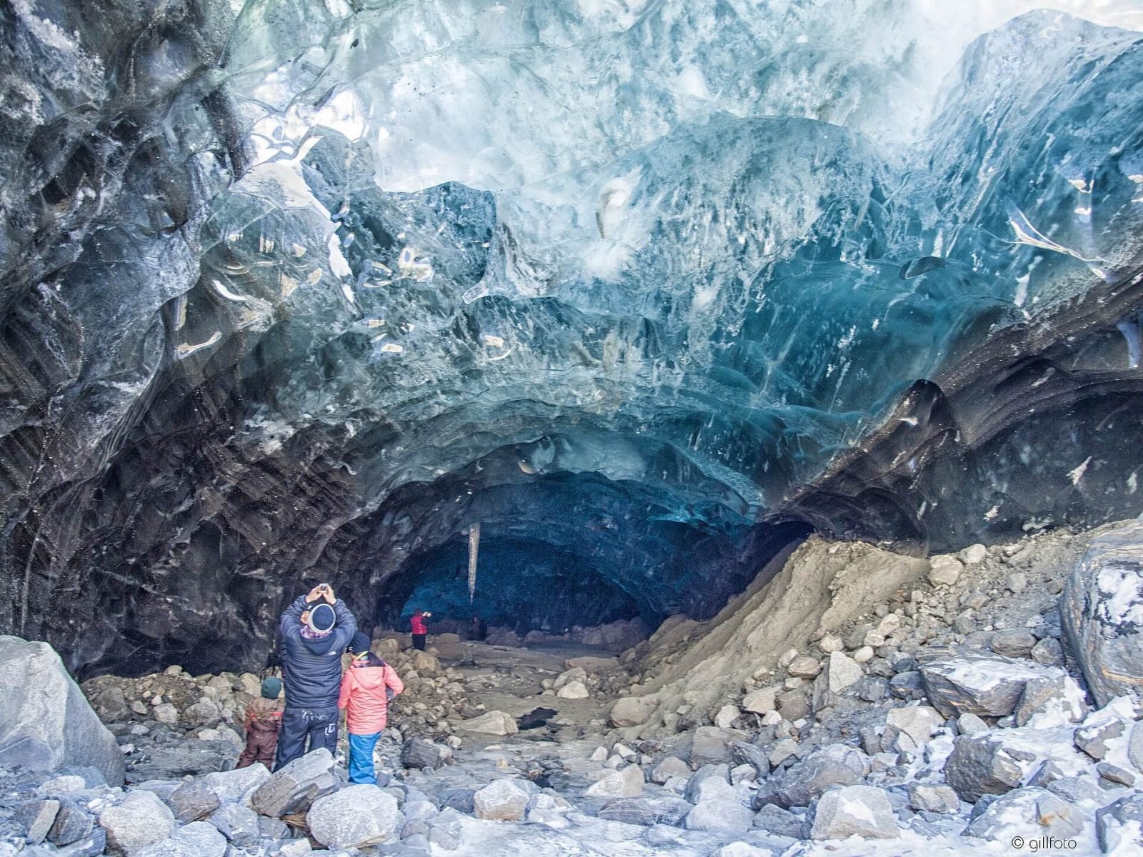 Two visitors standing inside a Mendenhall Glacier ice cave beneath a ceiling of blue ice