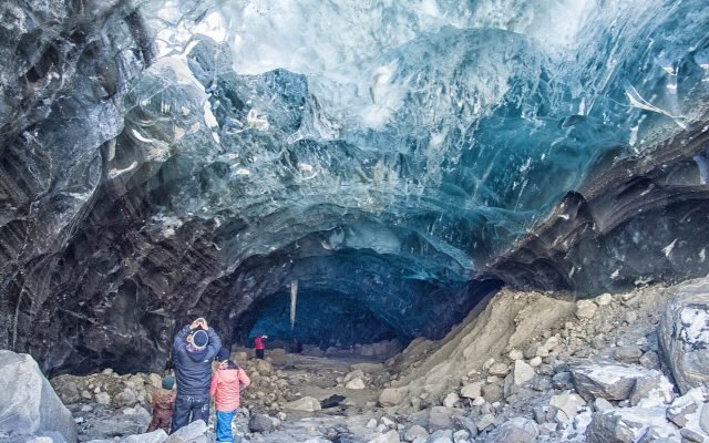 Two visitors standing inside a Mendenhall Glacier ice cave beneath a ceiling of blue ice