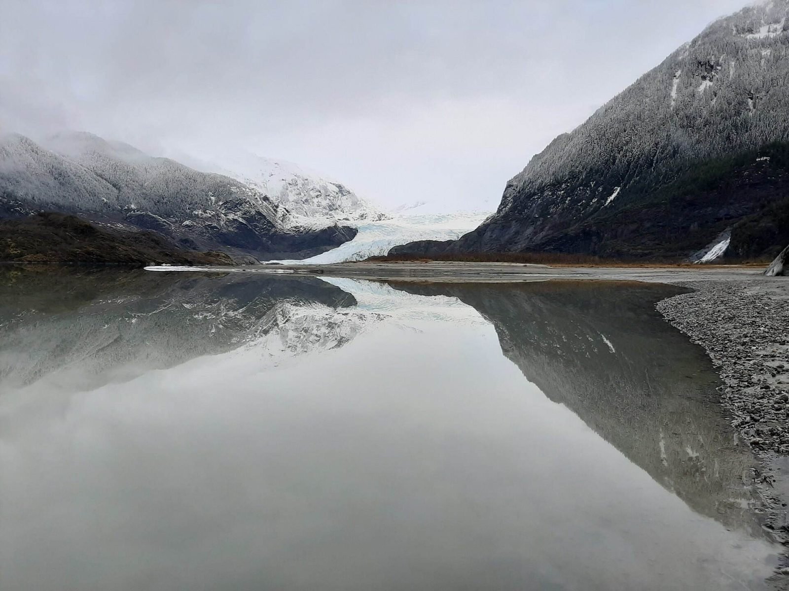 Mendenhall Glacier and snow-dusted mountains reflected in the still lake on a grey winter day