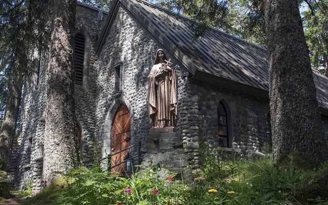 The stone chapel of the Shrine of St. Therese among tall spruce trees