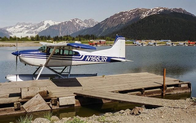 A floatplane moored at a wooden dock below snowy mountains