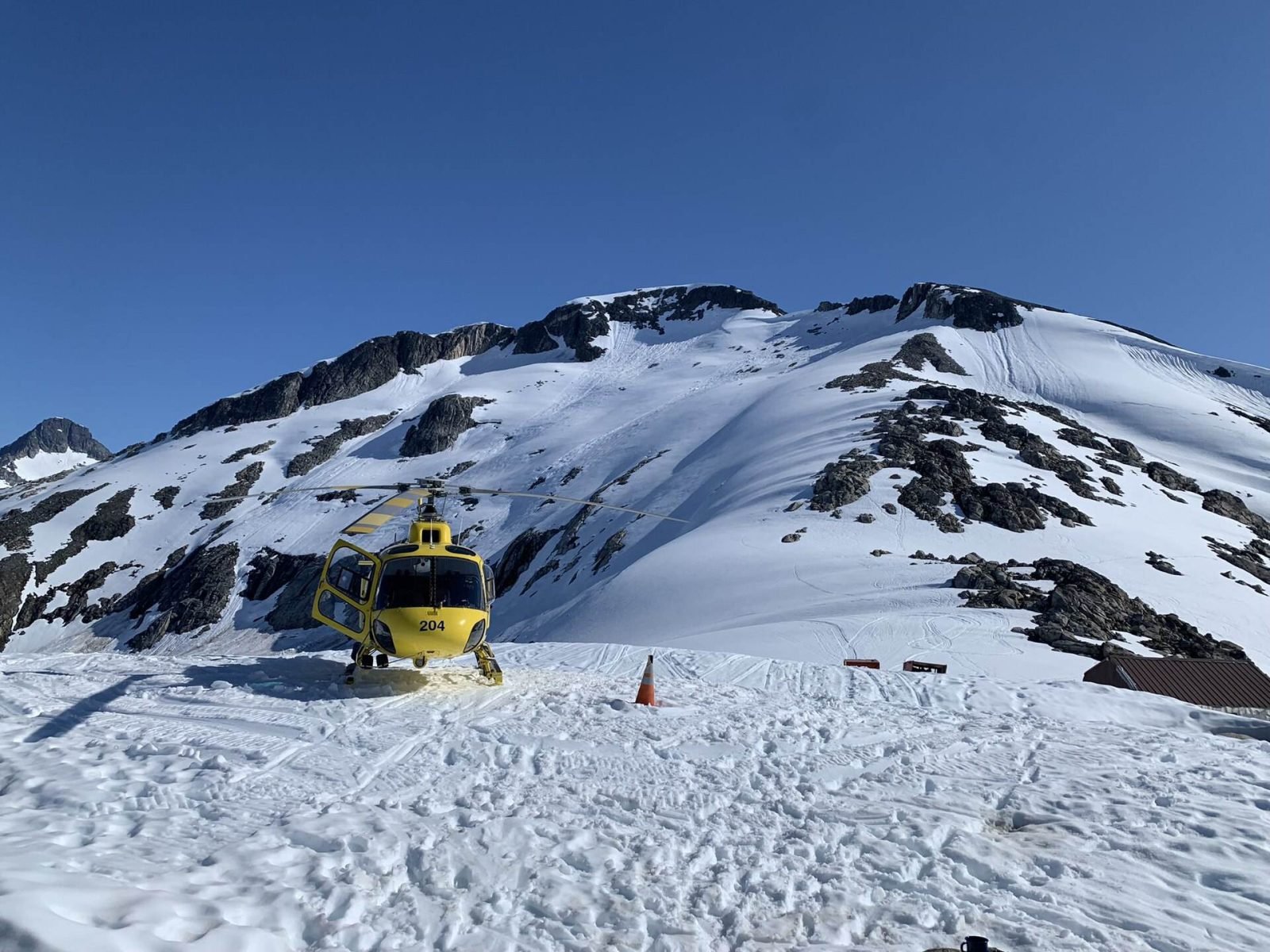 A yellow helicopter parked on the snowfield of the Juneau Icefield under a clear sky