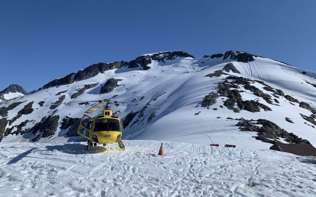 A yellow helicopter parked on the snowfield of the Juneau Icefield under a clear sky