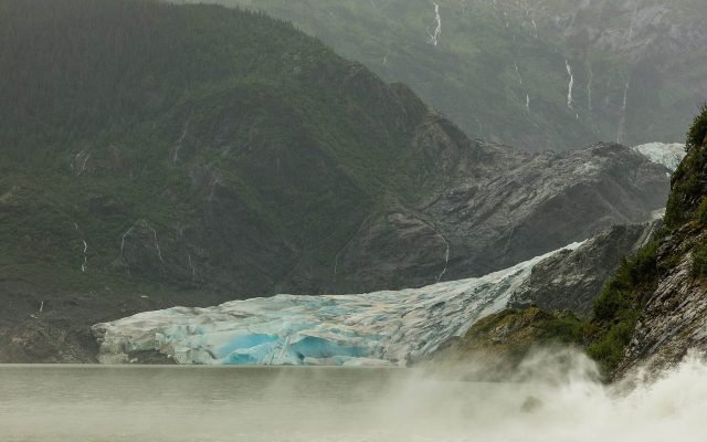 The blue-white face of Mendenhall Glacier meeting the lake below forested mountains