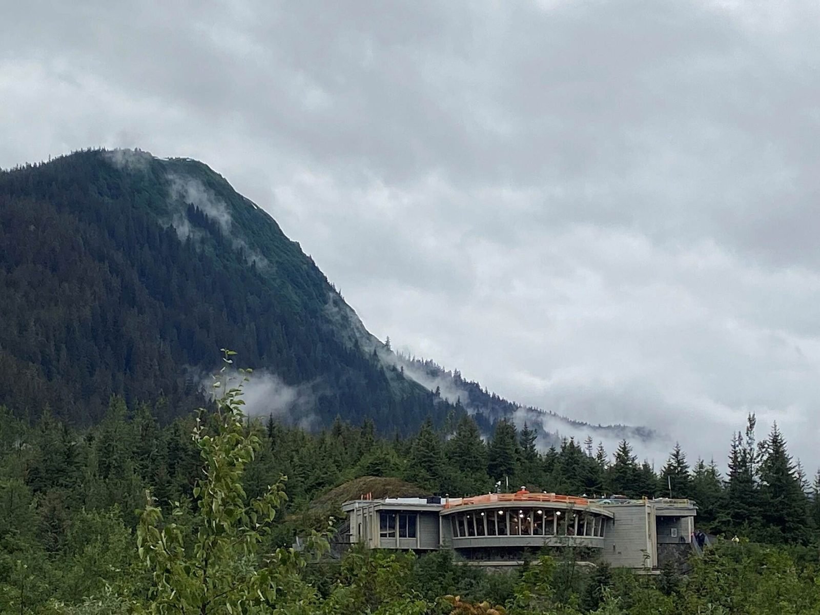 The Mendenhall Glacier Visitor Center on a forested ridge below misty mountains